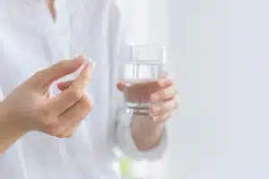 錠剤と水の入ったコップを手に持つ服薬イメージ（生成画像・実際の製品とは異なります）